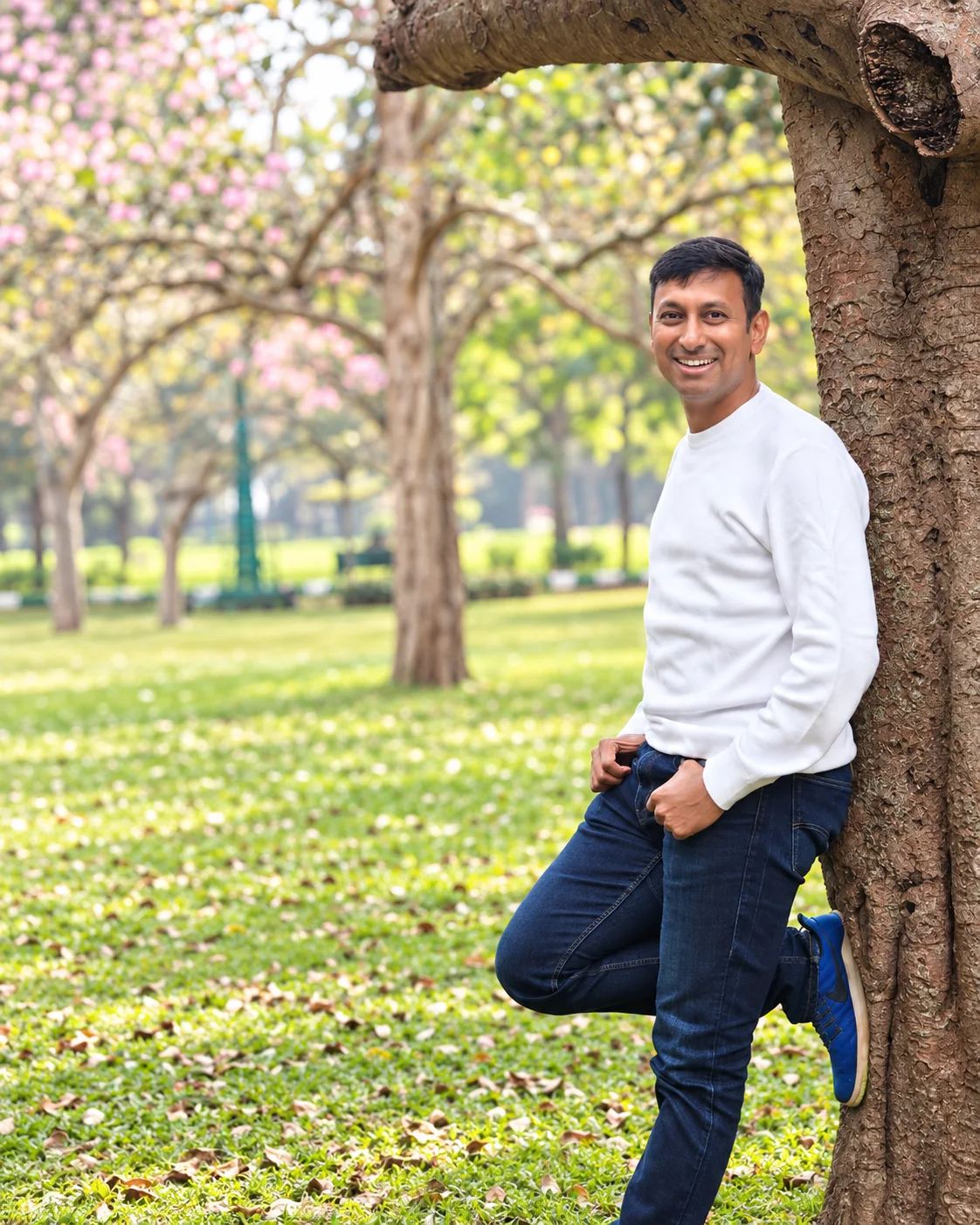Manjunath smiling in sunlight beside a tree in a green park